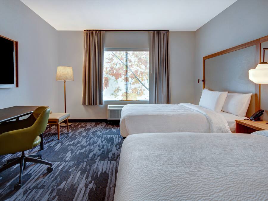 A hotel room with two beds, a desk, a chair, a lamp, and a window with curtains.
