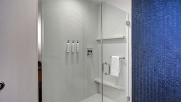 Un baño moderno con cabina de ducha de vidrio, paredes con azulejos blancos y cortina de ducha azul con textura.