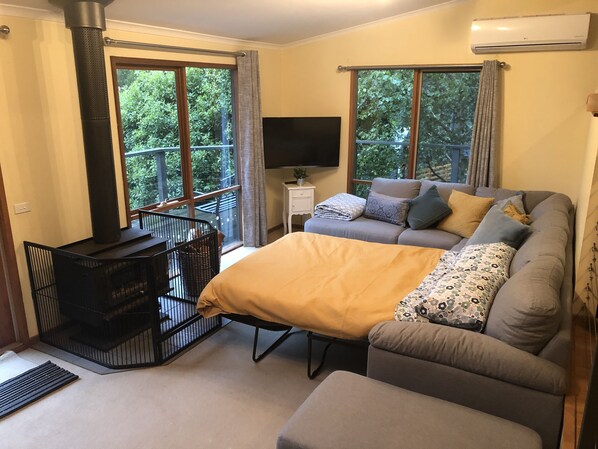 A cozy room with a sofa, a TV, a fireplace, and large windows.