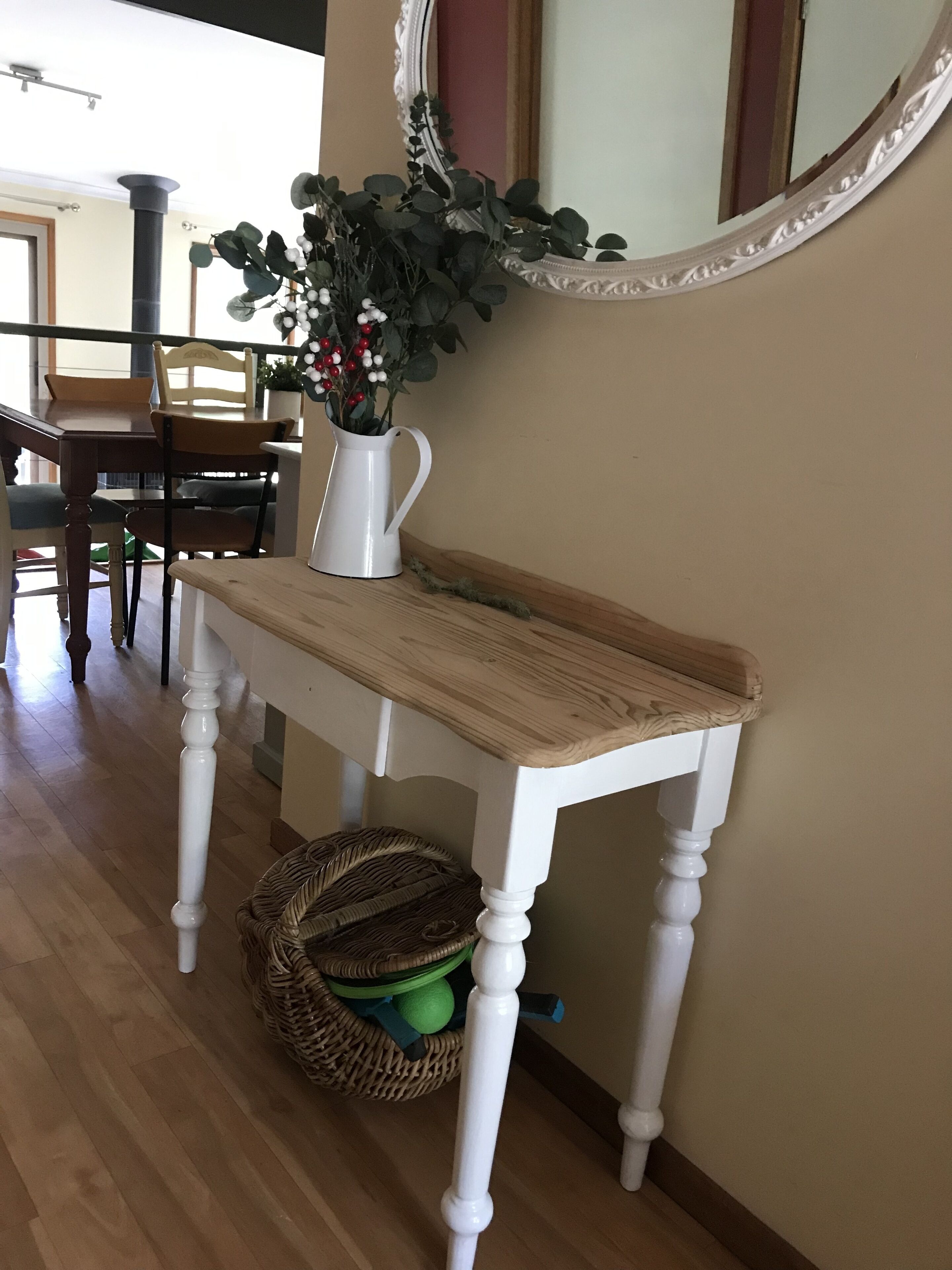 Une console en bois blanc, dotée d'un plateau en fibres tressées, avec un panier en osier placé en dessous et une plante en pot ornée de baies rouges.