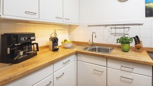 Een moderne keuken met witte kasten, een koffieapparaat, een spoelbak en een klok aan de muur.