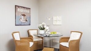 Een kamer met een ronde glazen tafel, twee rieten stoelen, een kleine witte vaas met bloemen, een poster aan de muur en een 'LOVE'-bord.