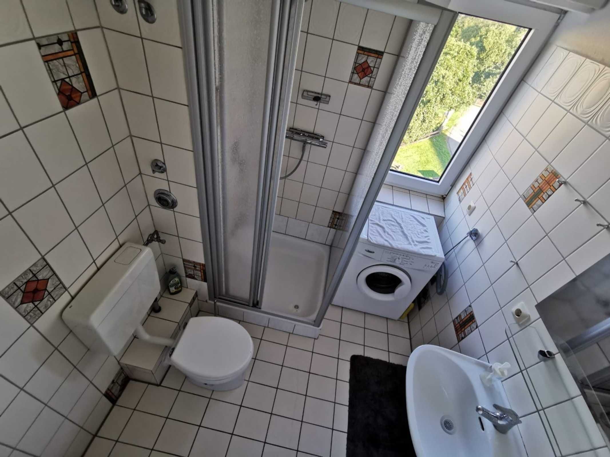 A compact bathroom with a toilet, shower, and washing machine.