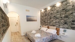 Un dormitorio con pared de piedra, una cama con colcha estampada, un banco de madera y un cuadro en la pared.