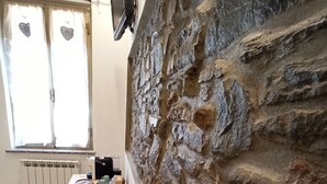 Una cocina con pared de piedra, mesa de madera y ventana con cortinas.