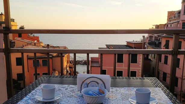 Un balcón con una mesa para dos, con vista a un paisaje urbano costero.