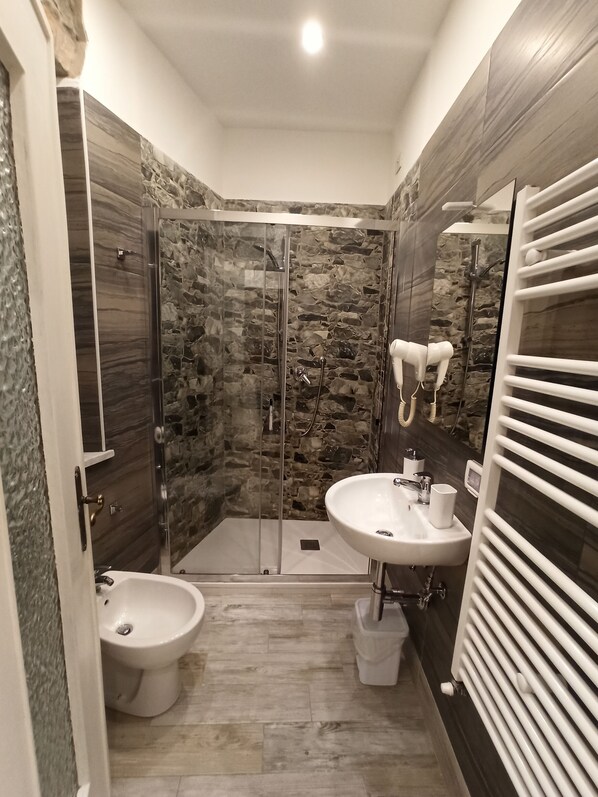 A modern bathroom with a glass-enclosed shower, a pedestal sink, and a bidet.
