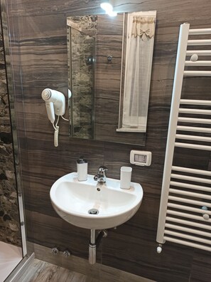 A bathroom with a marble wall, a white sink, a hairdryer, a towel rack, and a mirror.