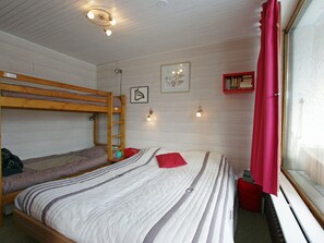 A dormitory room with bunk beds, a bed with striped bedding, a red curtain, and a window with blinds. - 2-bedroom apartment with balcony in Tignes (Tignes-Le Lavachet)