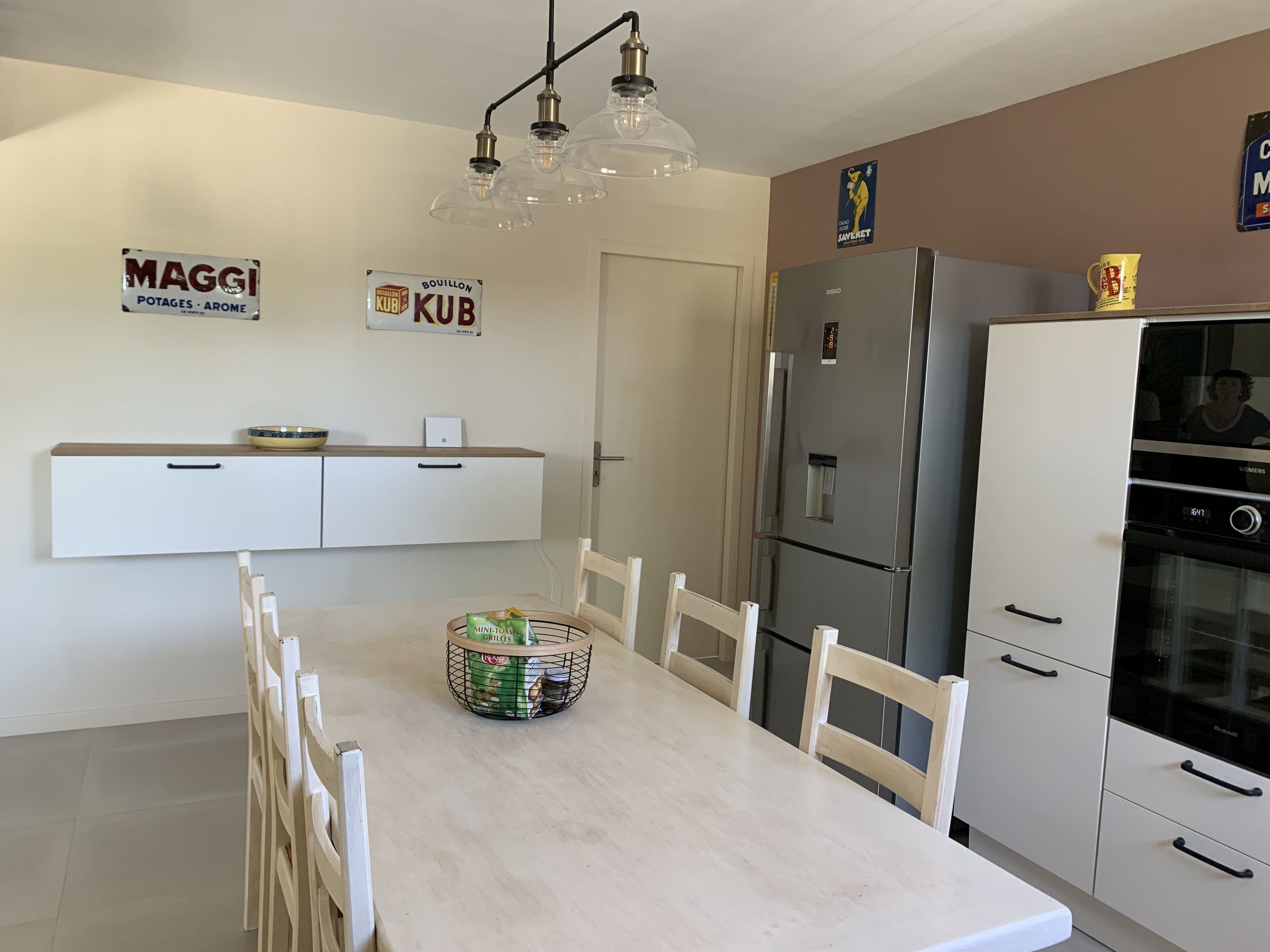 Une cuisine moderne avec des meubles blancs, un réfrigérateur en acier inoxydable et une table à manger avec des chaises.