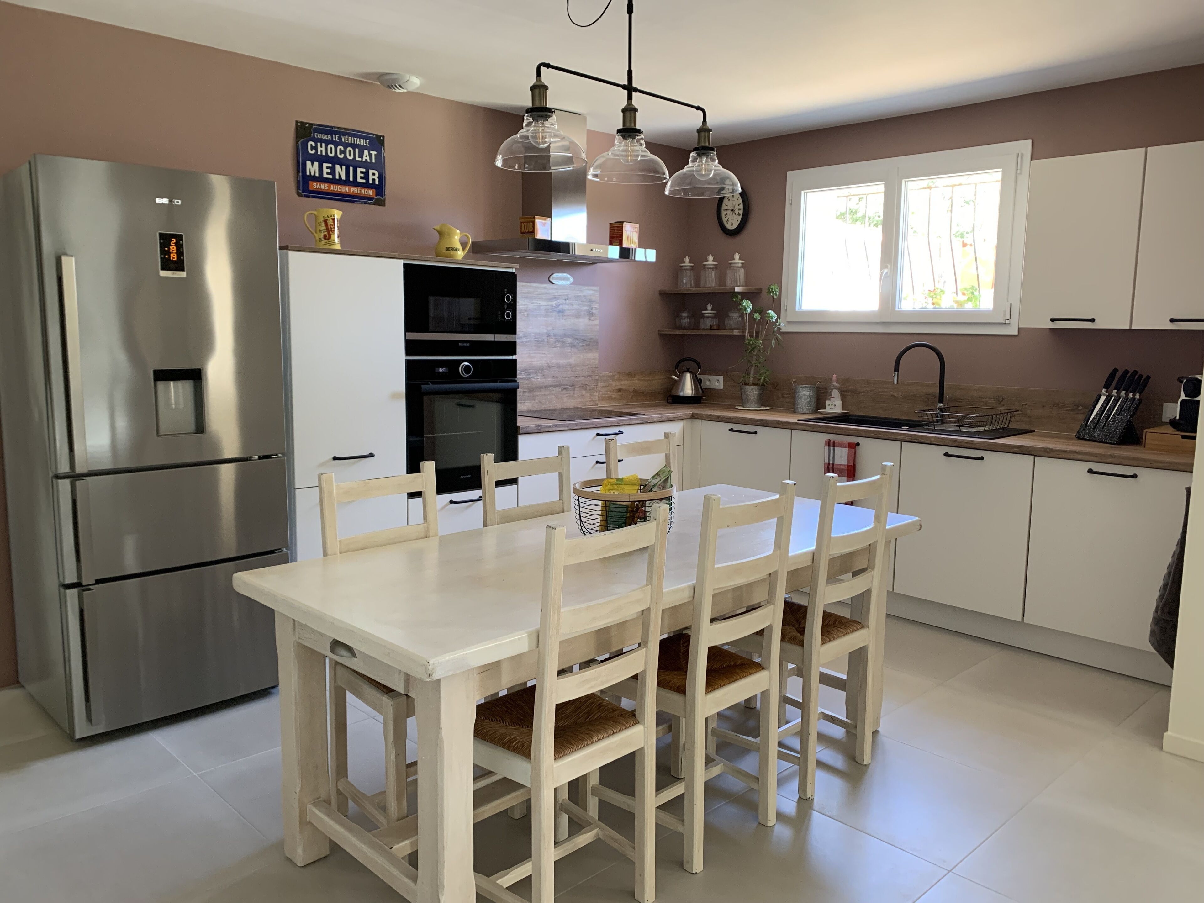 A modern kitchen with a stainless steel refrigerator, a built-in oven, and a dining area with a white table and chairs.