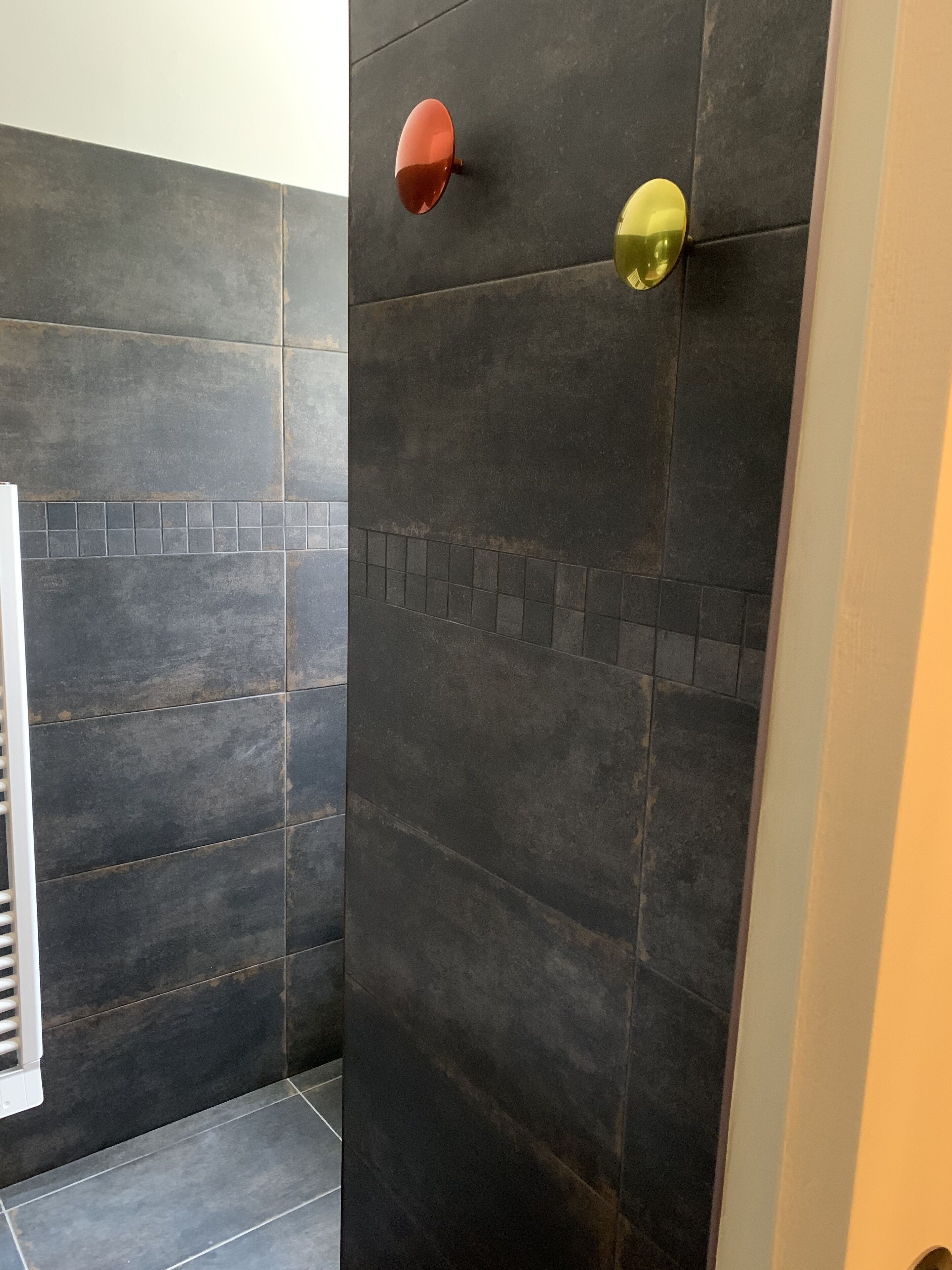Un baño con paredes de azulejos oscuros y un toallero blanco.
