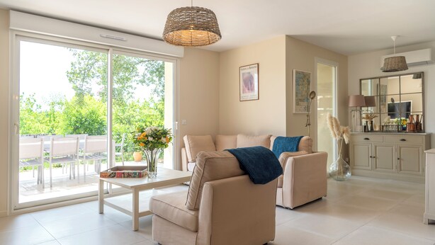 Amplia sala de estar con sofá y sillón, una mesa de comedor con un jarrón de flores, y un área de cocina con armarios y televisor.