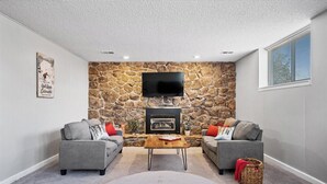 Ein Wohnzimmer mit einer Steinwand, einem Kamin, zwei grauen Sofas, einem Couchtisch und einem Wand-Fernseher.