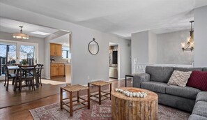 A spacious living room with a grey sofa, a round wooden coffee table, and a dining area with a wooden table and chairs.