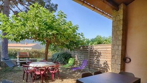 An outdoor patio area with a round table and chairs, a wooden fence, and a tree providing shade. - Garden-Level Apartment, 3 Rooms, 6 Guests, Near Liscia Beach (Calcatoggio)