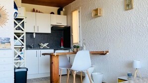 Una cocina compacta con armarios blancos, una mesa de madera y una silla blanca.