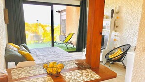 Un área de comedor con una mesa dispuesta para dos personas, un frutero y vistas a un balcón con una silla y un televisor.