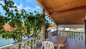 A covered balcony with a table and chairs, a stone pillar, and a view of neighboring buildings. - Nice, quiet, and inexpensive family apartment with proximity to sandy beach (Privlaka)