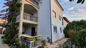 A two-story building with a balcony, a stone entrance, and a garden with potted plants and flowers. - Nice, quiet, and inexpensive family apartment with proximity to sandy beach (Privlaka)