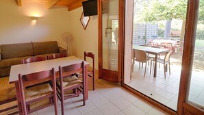 A cozy room with a wooden ceiling, a sofa, a dining table with chairs, and a sliding glass door leading to an outdoor patio area.