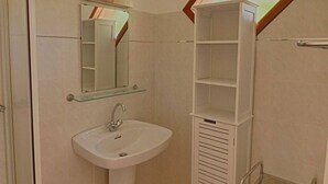 A bathroom with a pedestal sink, a mirror above it, and a built-in shelving unit.