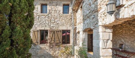 A stone building with a courtyard, featuring arched doorways and wooden shutters.