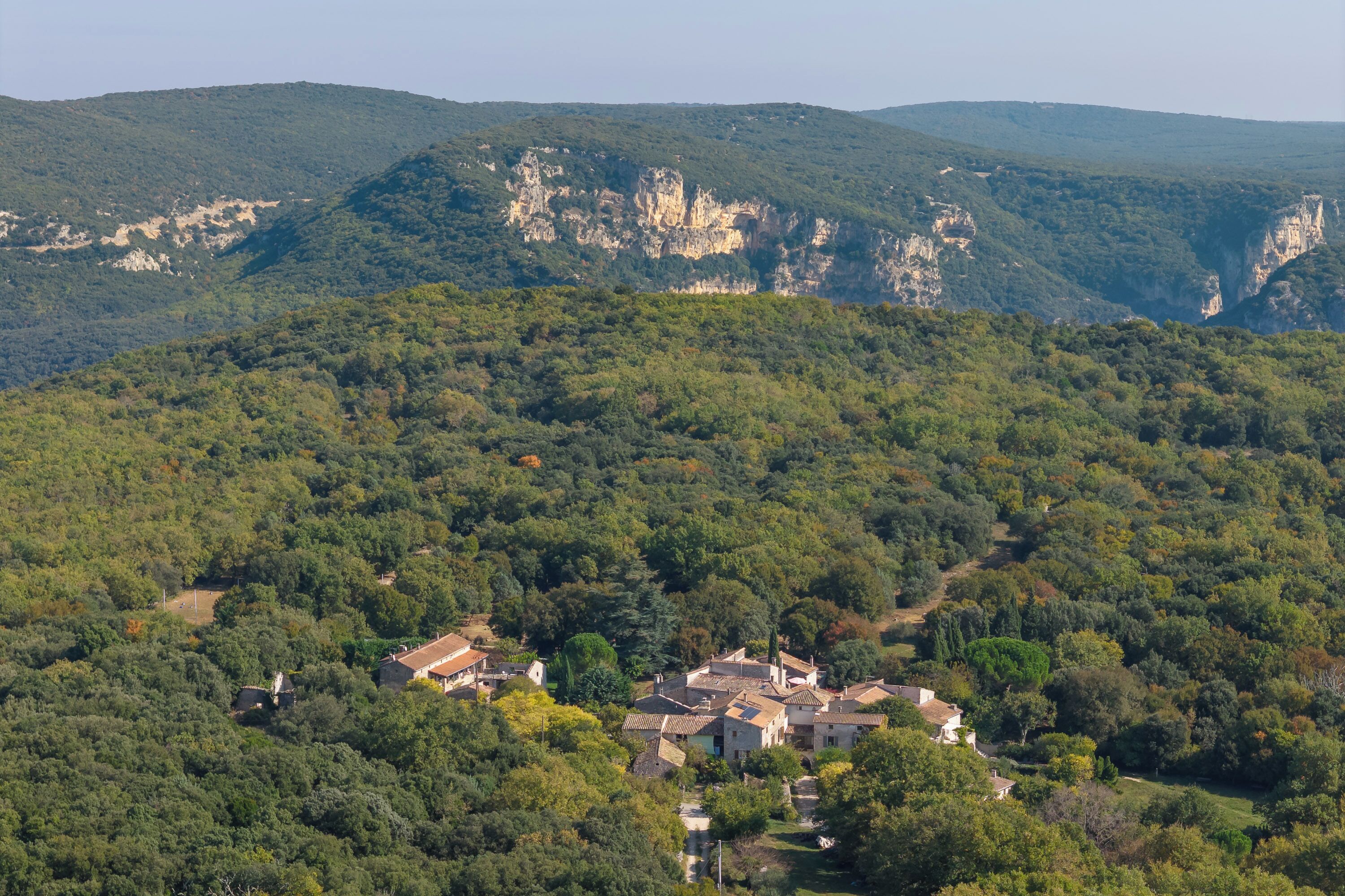 Un village niché dans une vallée, avec des bâtiments traditionnels entourés d’une forêt dense et de falaises.