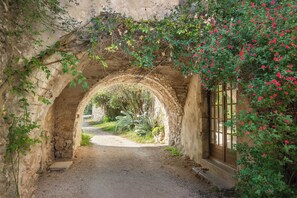 Un sentier en pierre en forme d’arche mène à un bâtiment rustique doté d’une porte en bois et d’une fenêtre.
