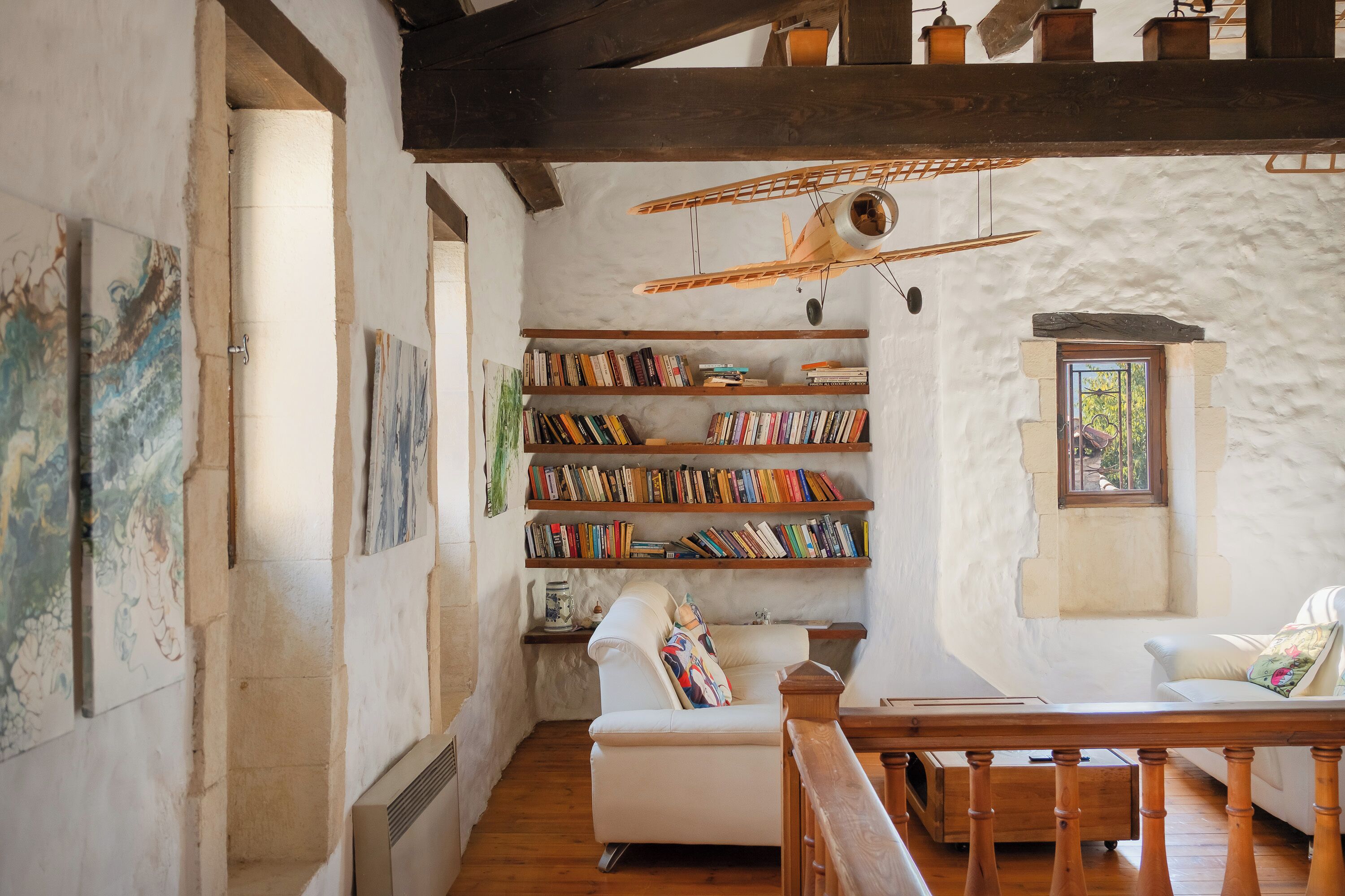 Une pièce chaleureuse avec un canapé blanc, des étagères en bois remplies de livres, une petite table et une poutre en bois au plafond.