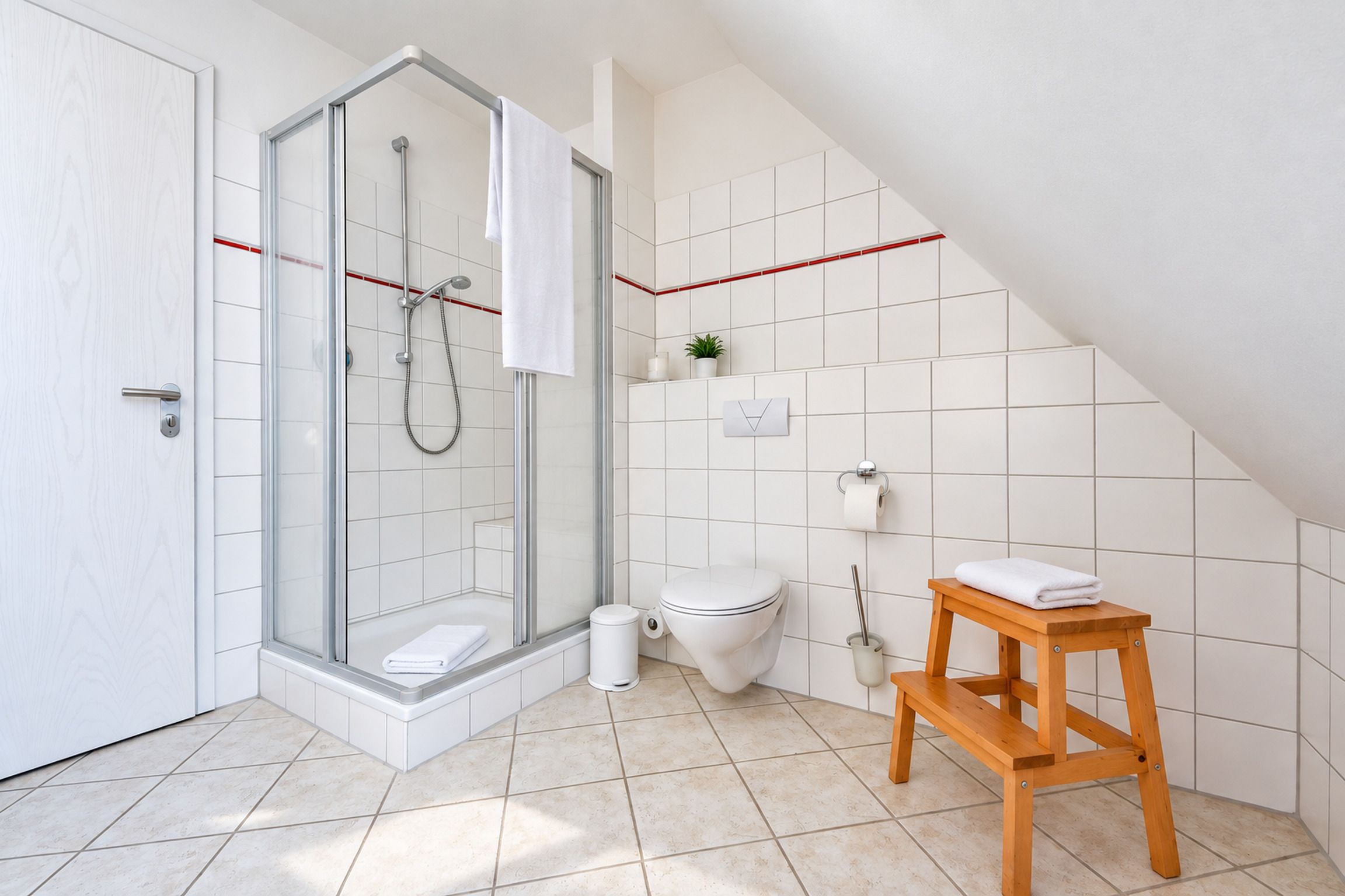 A modern bathroom with a glass shower enclosure, a toilet, and a wooden stool.