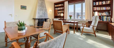 Una habitación con chimenea, una mesa de comedor, sillas, una estantería y una ventana con cortinas.