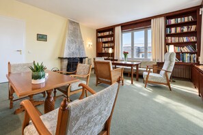 Ein Zimmer mit Kamin, einem Esstisch, Stühlen, einem Bücherregal und einem fenster mit Vorhängen.