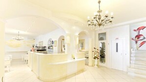 A spacious lobby with a reception desk, a chandelier, and a large painting of flowers. - Hotel Gioiosa (Cesenatico)