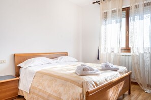 A neatly made bed with a wooden headboard, a bedside table, and a window with sheer curtains.