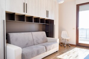 A modern living room with a grey sofa, wooden cabinets, a white chair, and a wooden floor.