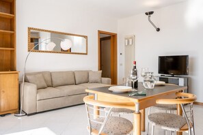 A living room with a sofa, a dining table with chairs, a TV, and a mirror.