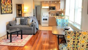 A compact living space with a sofa, a patterned armchair, a dining table, and a kitchen area with a microwave and stove.