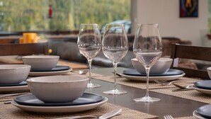 A dining table set with bowls, plates, and wine glasses, with a view of greenery outside. - Expansive Mountain Views - New Construction, Close to Town + PF, Fireplace, Pool Table, Deck (Grand Lake)