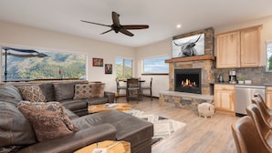 A spacious living room with a fireplace, leather sofa, and a dining area with a view of the mountains. - Expansive Mountain Views - New Construction, Close to Town + PF, Fireplace, Pool Table, Deck (Grand Lake)