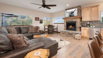 A spacious living room with a fireplace, leather sofa, and a dining area with a view of the mountains.