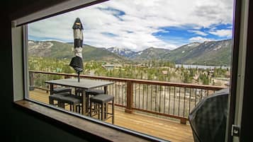 A balcony with a table and chairs, overlooking a mountainous landscape with a lake and buildings.