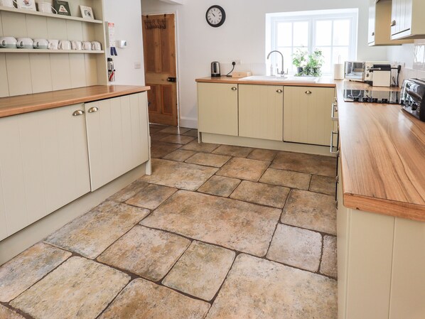 A kitchen with a stone tile floor, wooden countertops, and cream-colored cabinets. - The Old Post House at Low Stott Park (Ulverston)