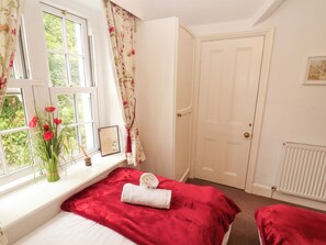 Um quarto com cama, janela com cortinas, porta e radiador.
