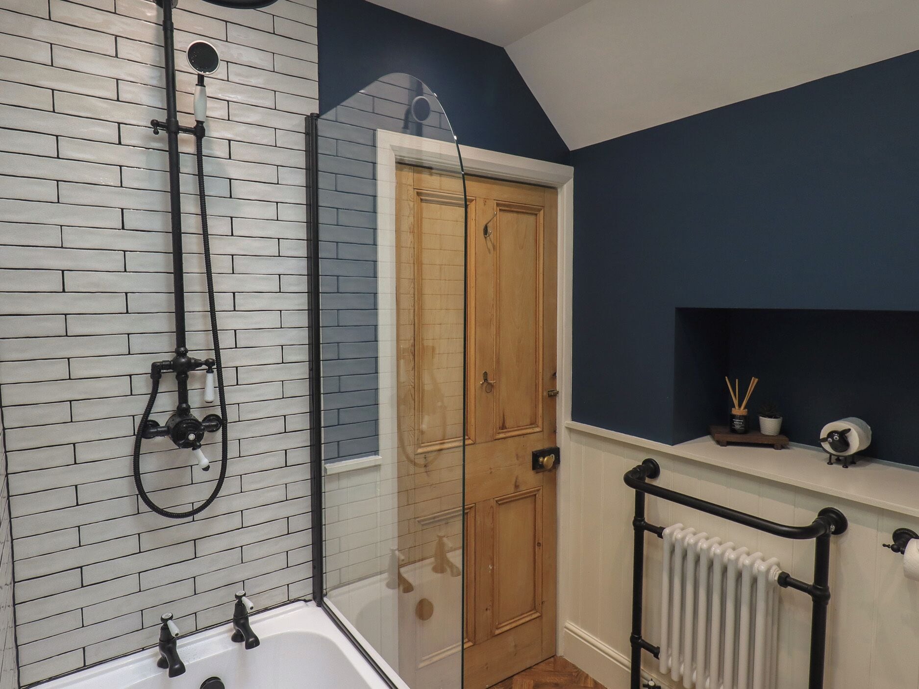Un baño con una bañera blanca, una ducha con manguera negra, una puerta de madera y un radiador blanco.
