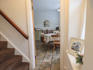 A staircase leading to a dining area with a table set for two, a kitchen area with a bread box, and a framed picture on the wall. - The Old Post House at Low Stott Park (Ulverston)