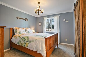 A bedroom with a wooden bed, a chandelier, a window with curtains, and a wall-mounted clock. - 🌻 Charming Cottage On Peaceful 5 Acres in the Mountains (Central Point)