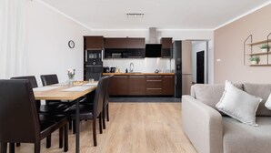 A modern kitchen with dark cabinets, a wooden dining table, and a grey sofa.