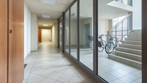 A hallway with a wooden door, tiled flooring, and a staircase with a bicycle parked nearby.