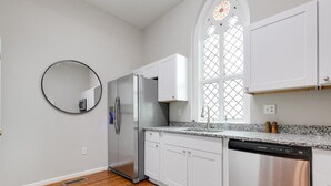 Una cocina moderna con armarios blancos, electrodomésticos de acero inoxidable, encimera de granito y un amplio ventanal con un diseño de vitral.